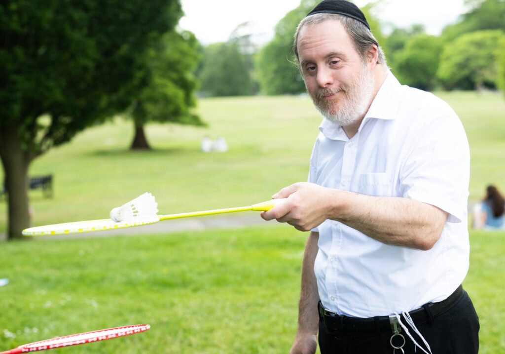 Person holding a badminton racket standing on a grassy field.