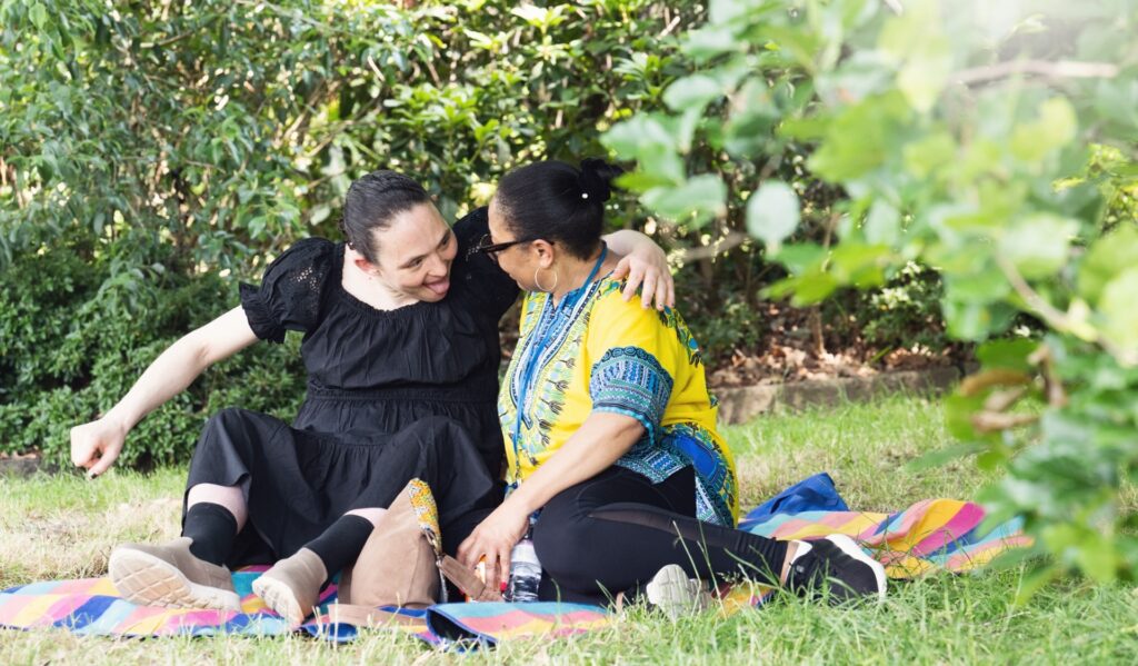 People sitting together outdoors on a picnic blanket in a garden, enjoying time together and building connections.