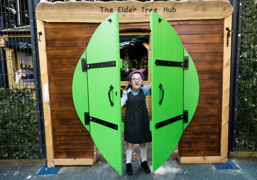Person standing in the doorway of The Elder Tree Hub outdoor learning space, opening bright green doors.