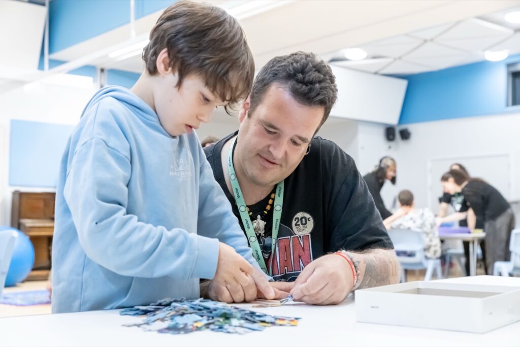 Child and adult working together on a jigsaw puzzle at a classroom table in an after school club.